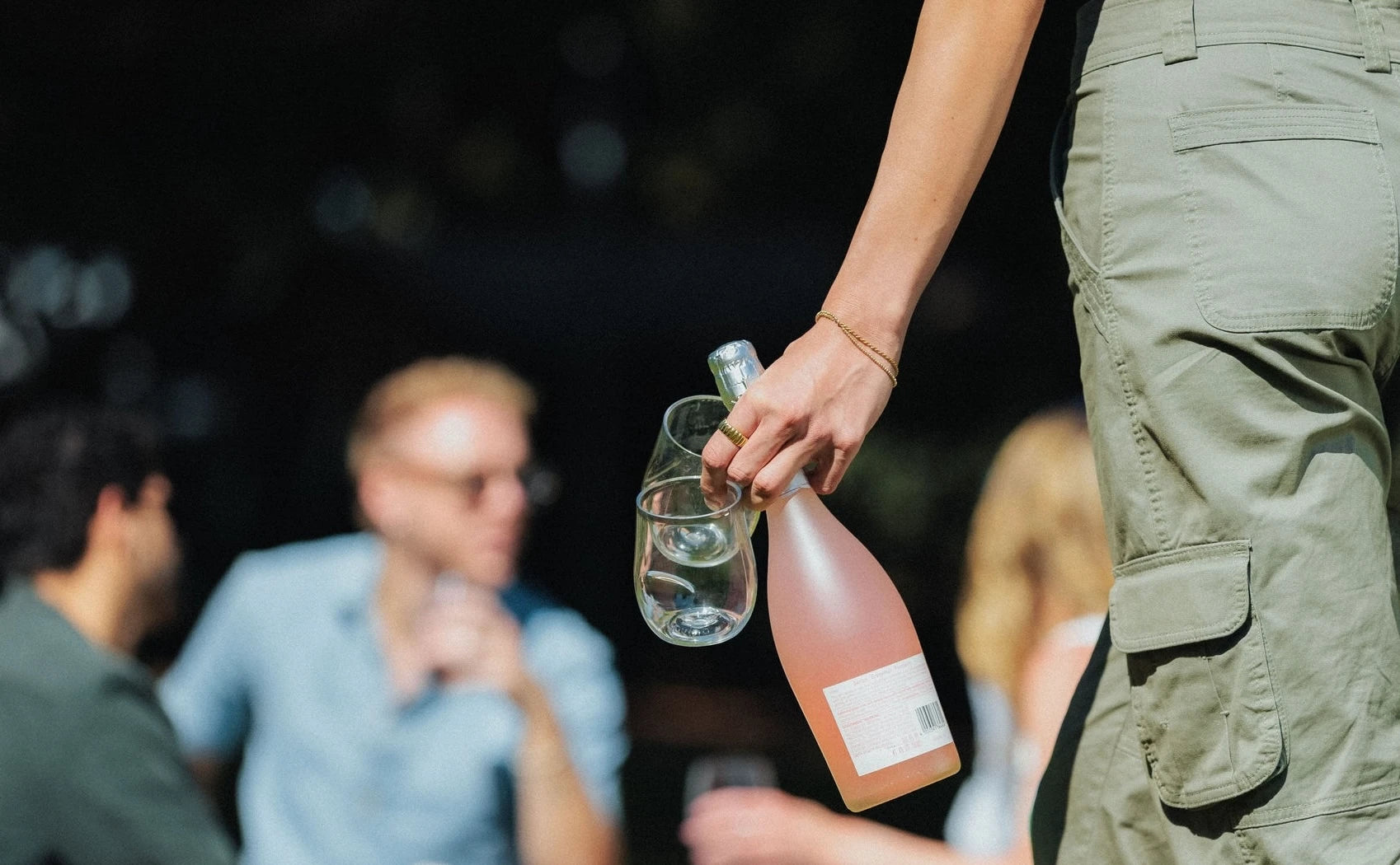 Two Govino shatterproof wine glasses carried with a bottle of rosé at an outdoor gathering